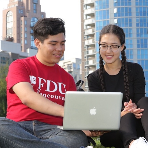 Three students sitting on the lawn looking at a laptop