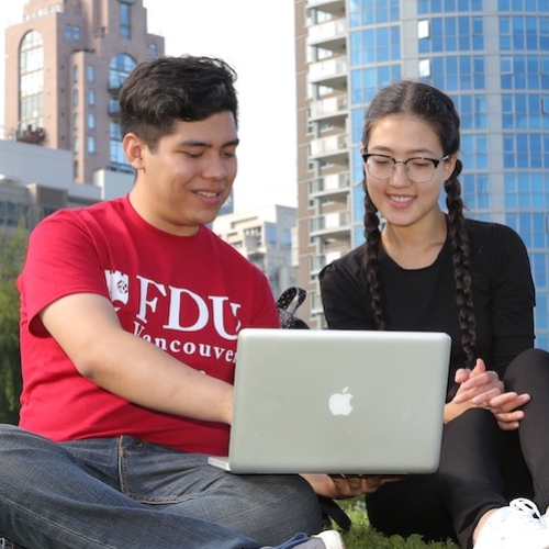 Three students sitting on the lawn looking at a laptop