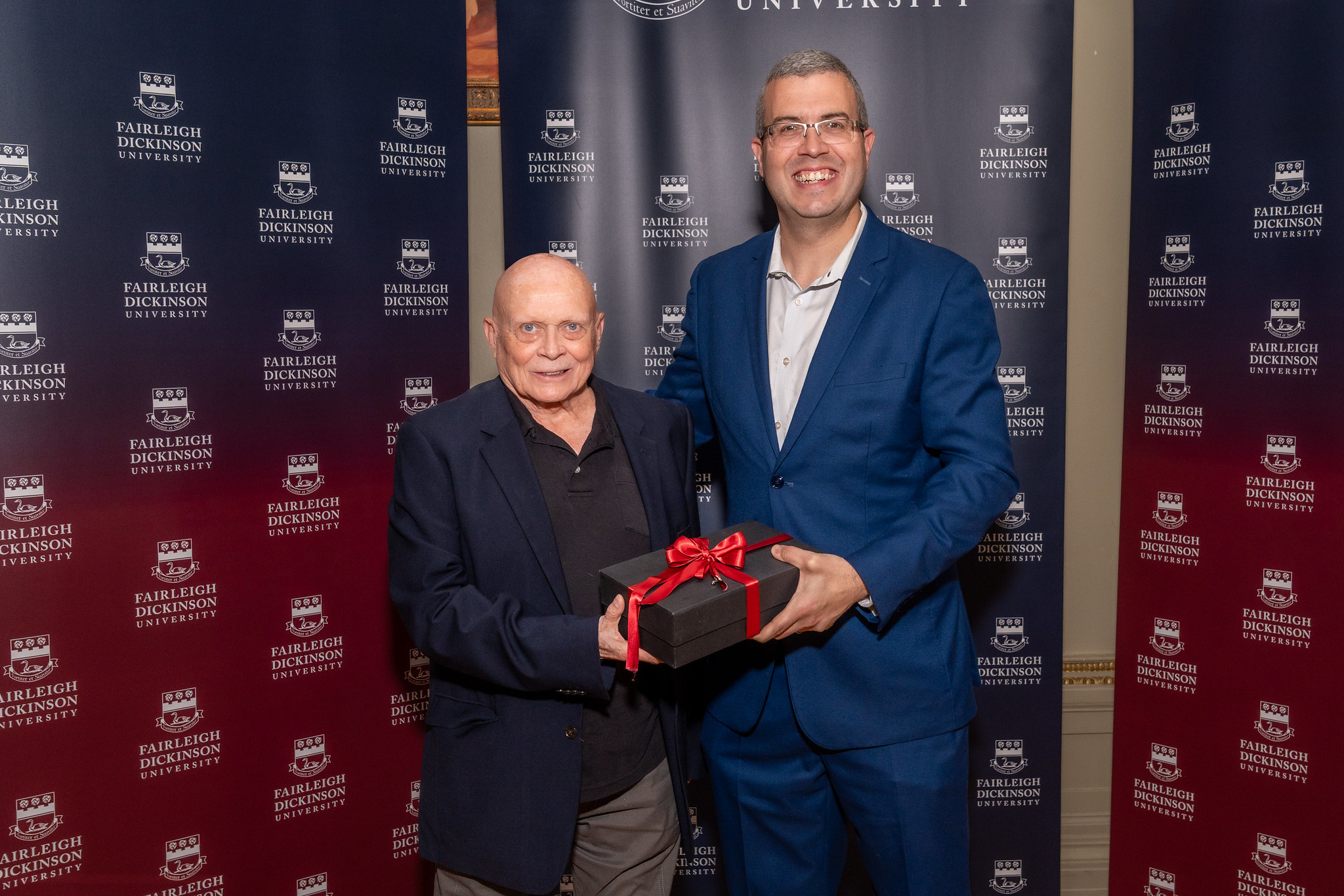 two men smile for the camera. they hold a present.