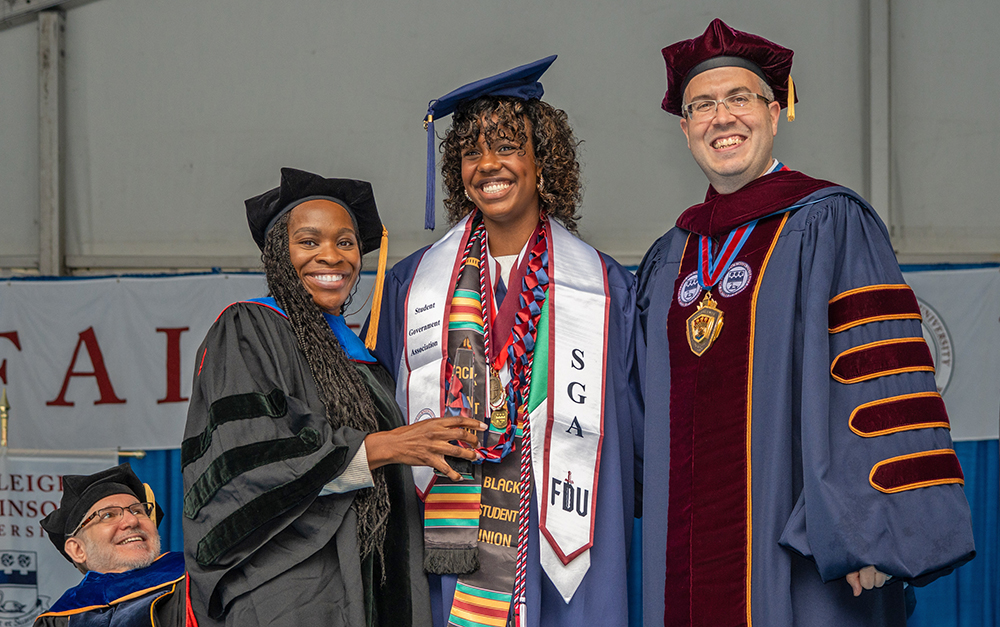 Three people dressed in caps and gowns smile for a photo.