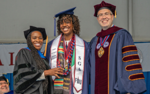 Three people dressed in caps and gowns smile for a photo.
