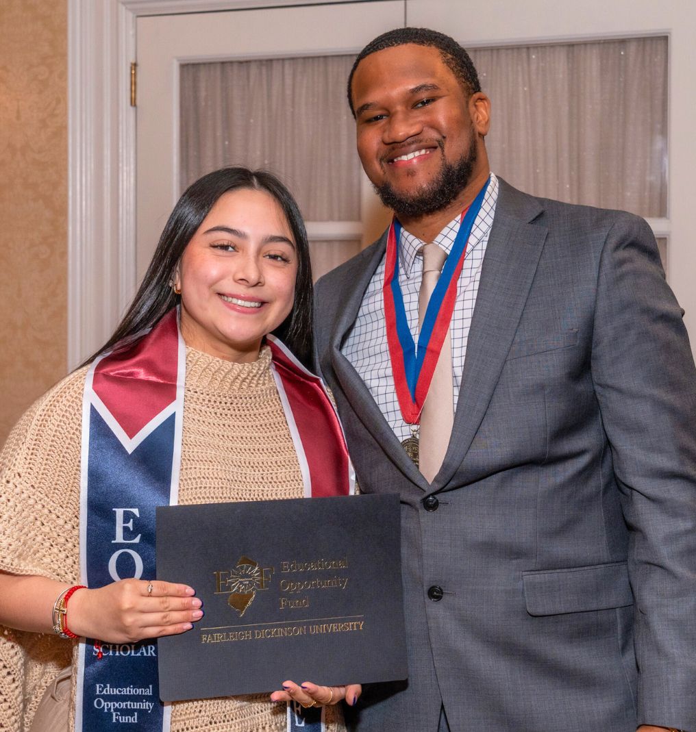 a student and a staff member smile for the camera. the student she holds up a certificate that read 