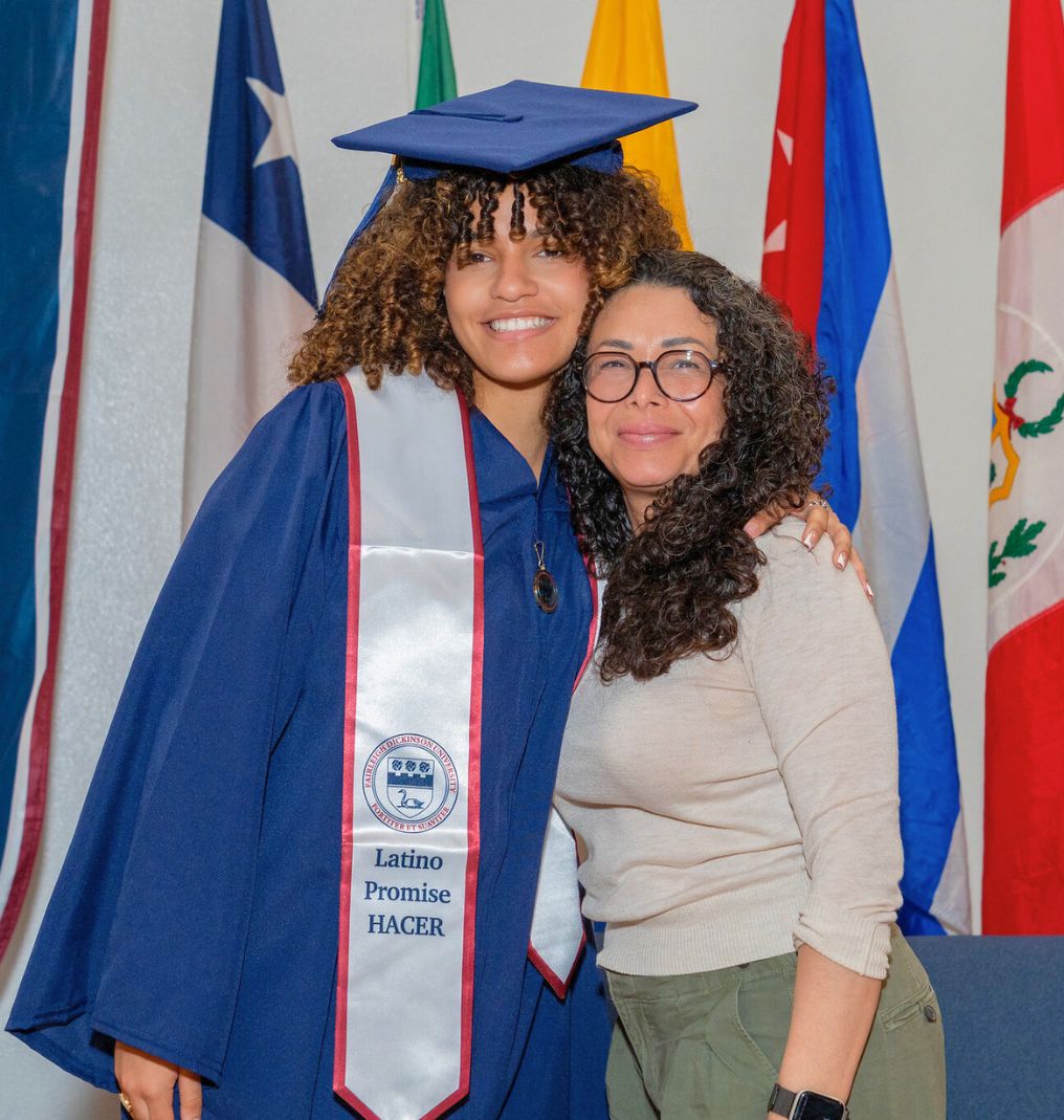 a graduating student and a staff member smile for the camera. the graduate wears a stole that reads 
