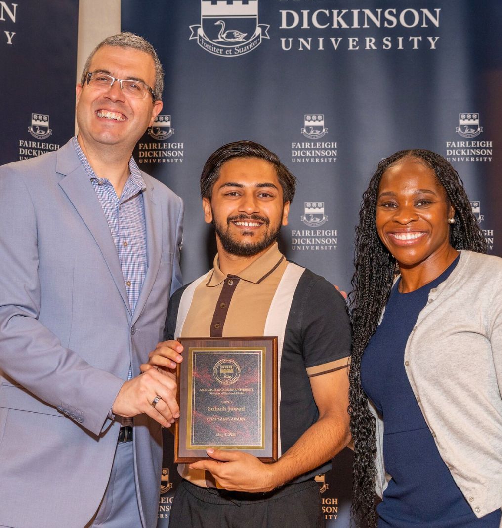 a student holds up an award and stands between FDU President Michael Avaltroni and Uchenna Baker.