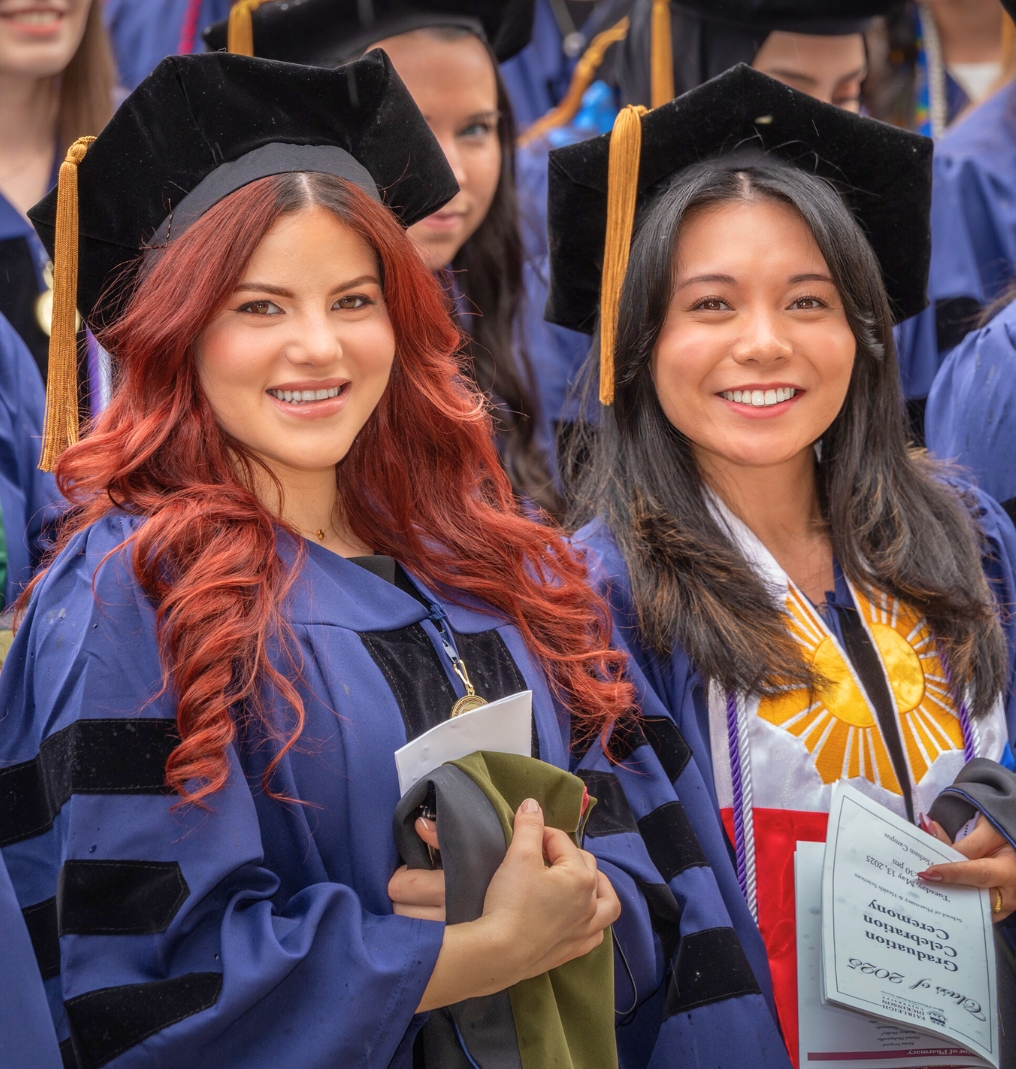 two doctoral graduates smile for the camera.