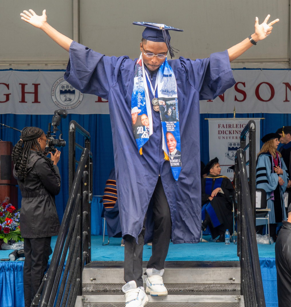 a graduate raises his arms in the air as he walks down the stairs from the commencement stage.
