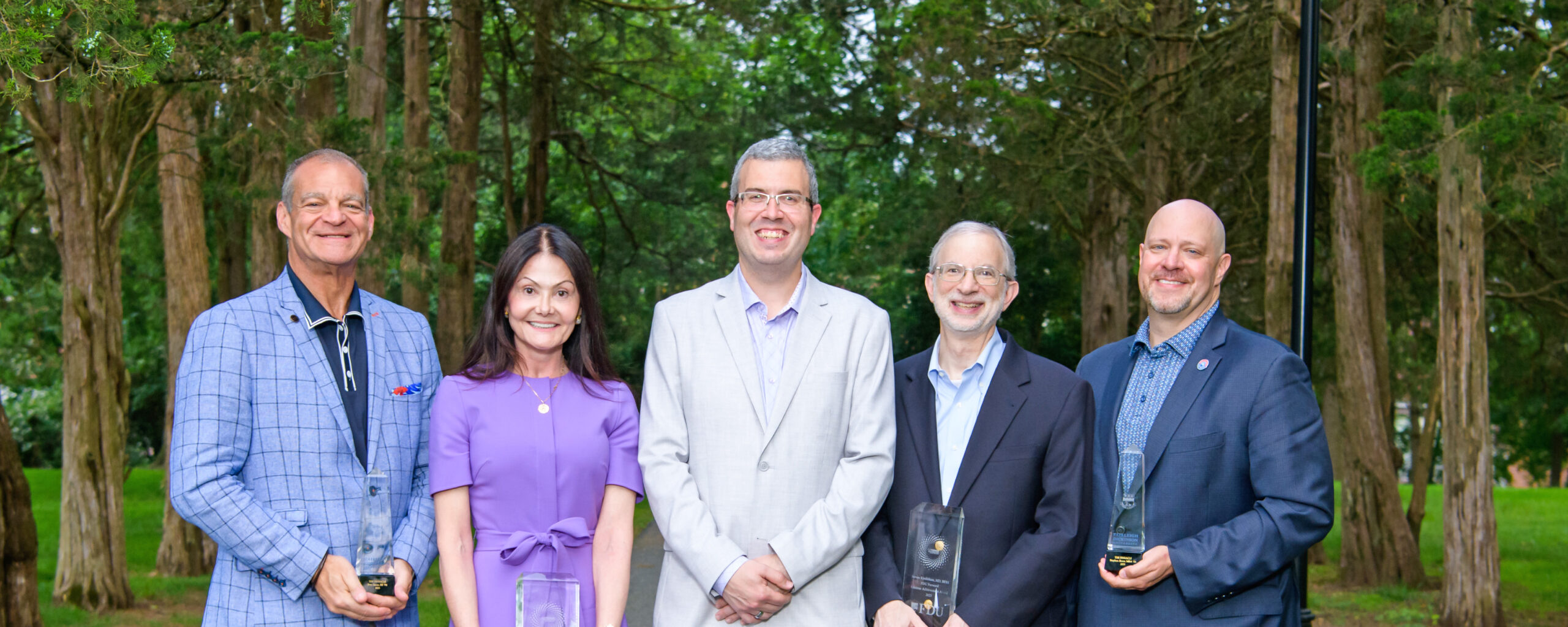 Four men and one woman in garden party attire stand in a row for a photo.