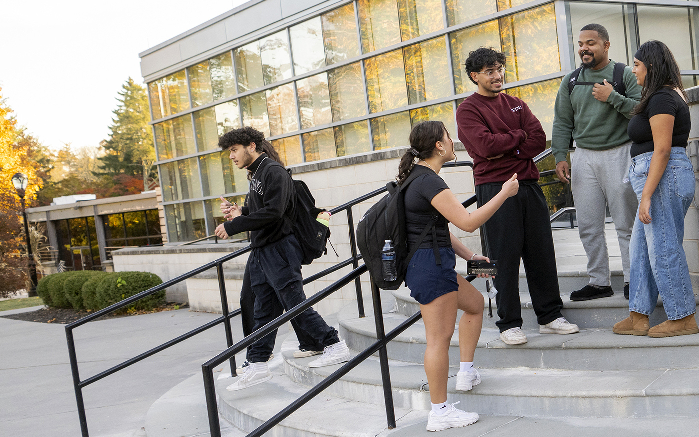A group of students stand on the steps outside of a campus library.