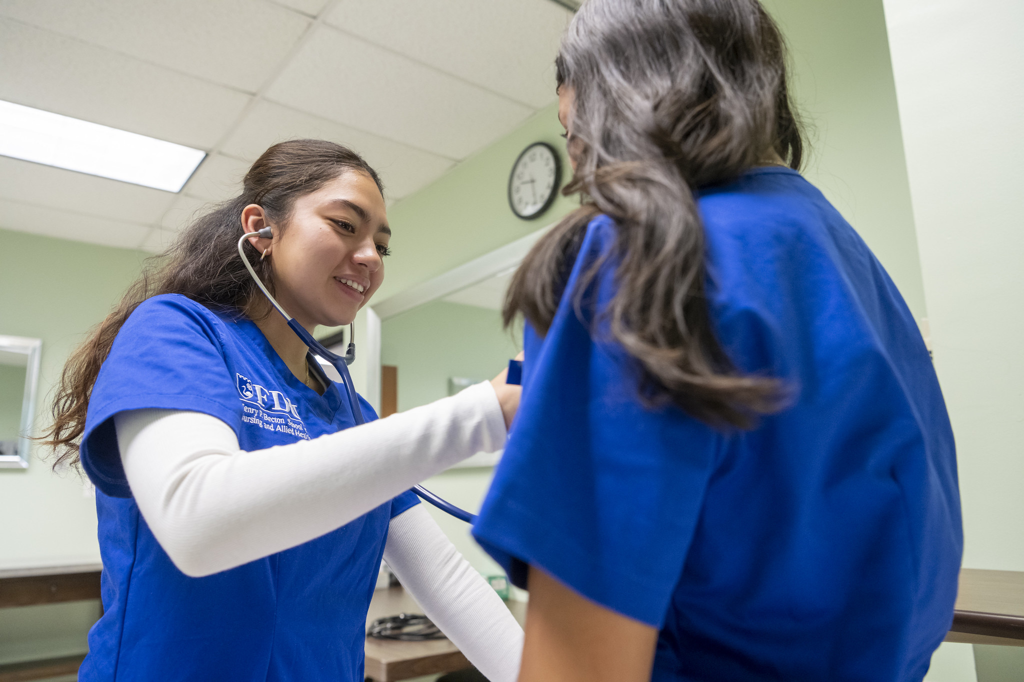 A student uses a stethoscope in class, examining another student.