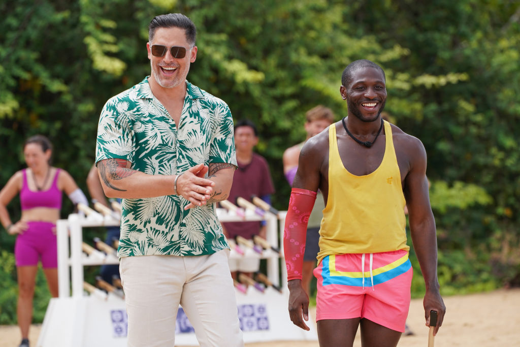Two men in bright summer clothing stroll on a beach on a reality tv show.