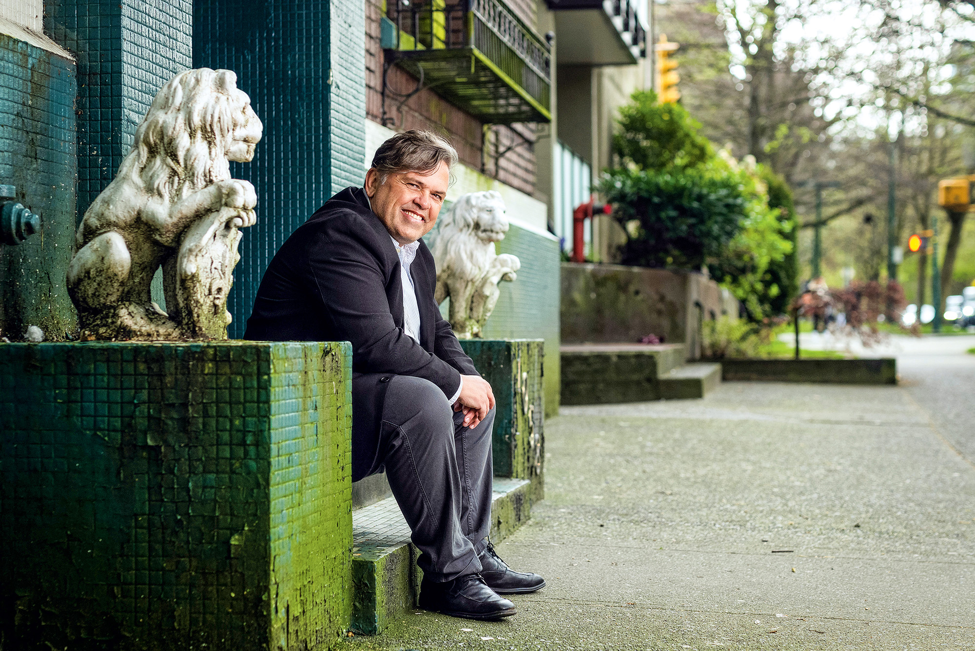 A man sits outside on a stoop flanked by lion statues.