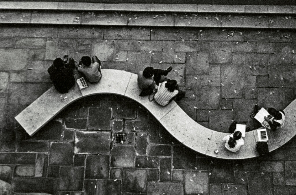 A vintage black and white photo from above of students sitting outside on a curved bench.
