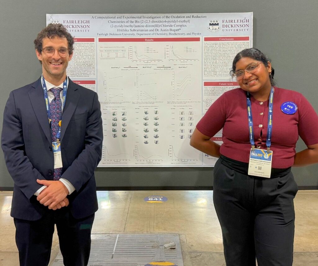 a college student and a professor smile for the camera. there is a poster board presentation behind them.