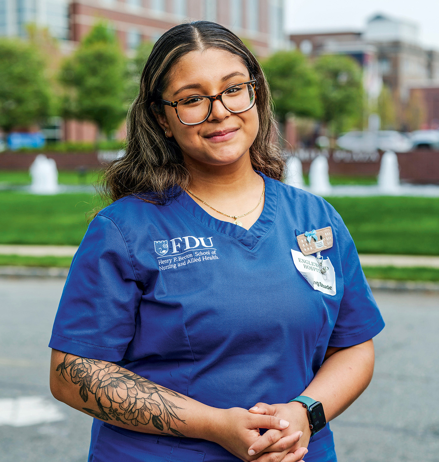 A female nursing student wearing scrubs stands outside her hospital clinical rotation.