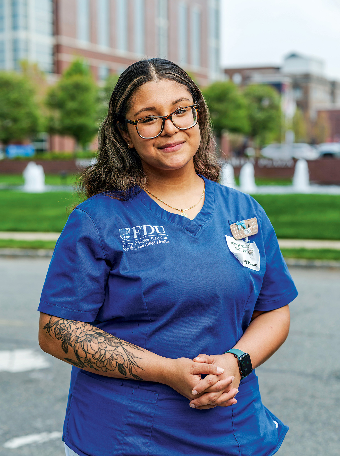 A female nursing student wearing scrubs stands outside her hospital clinical rotation.