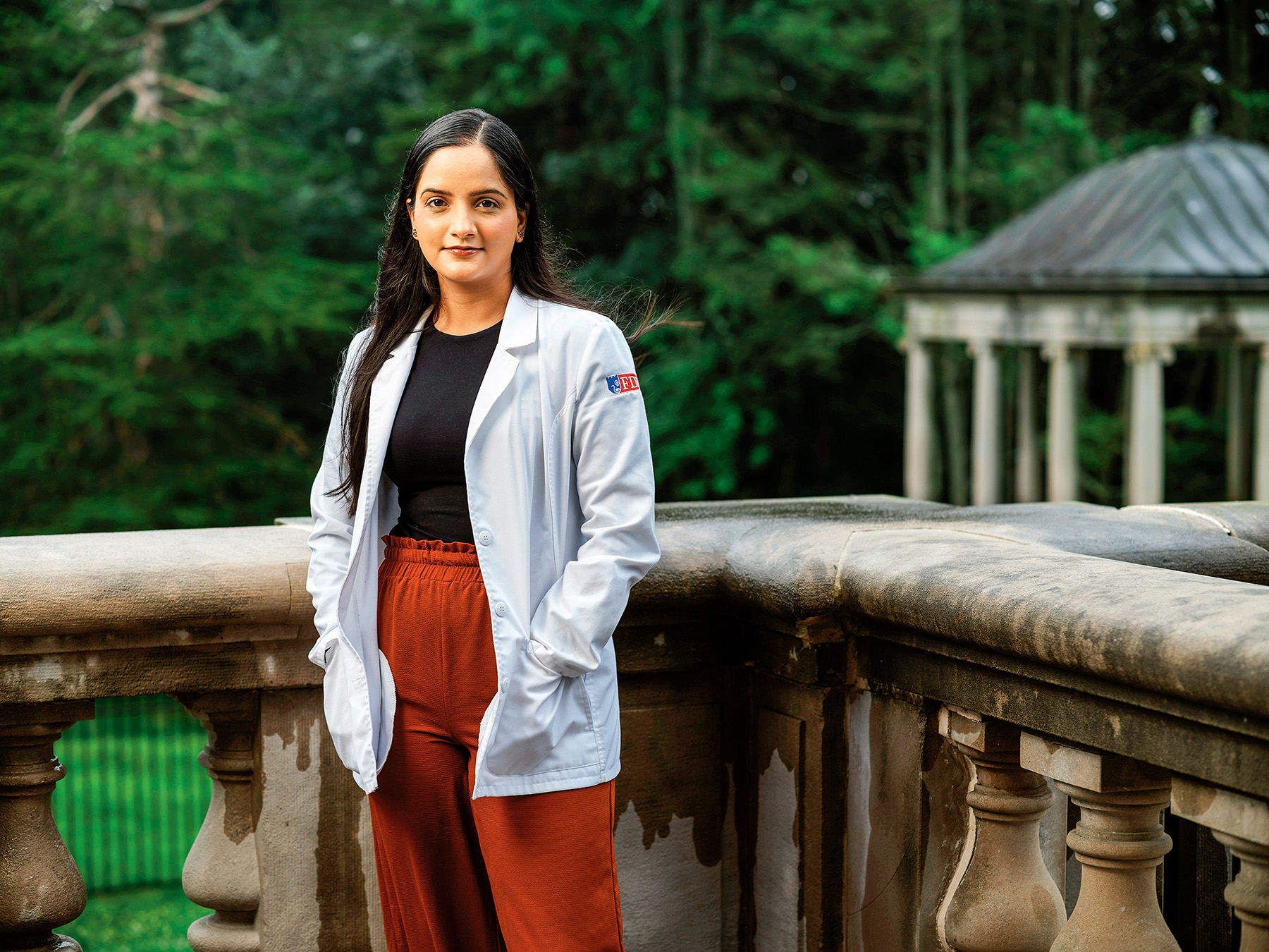A young woman in a white coat stands out on a terrace.