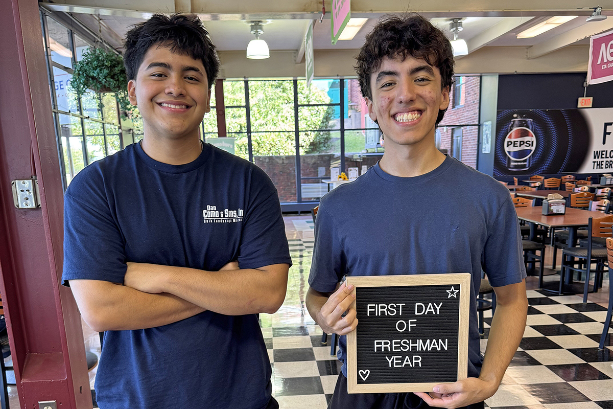 Two young men hold up a sign declaring that it's their first day of their freshman year of college.