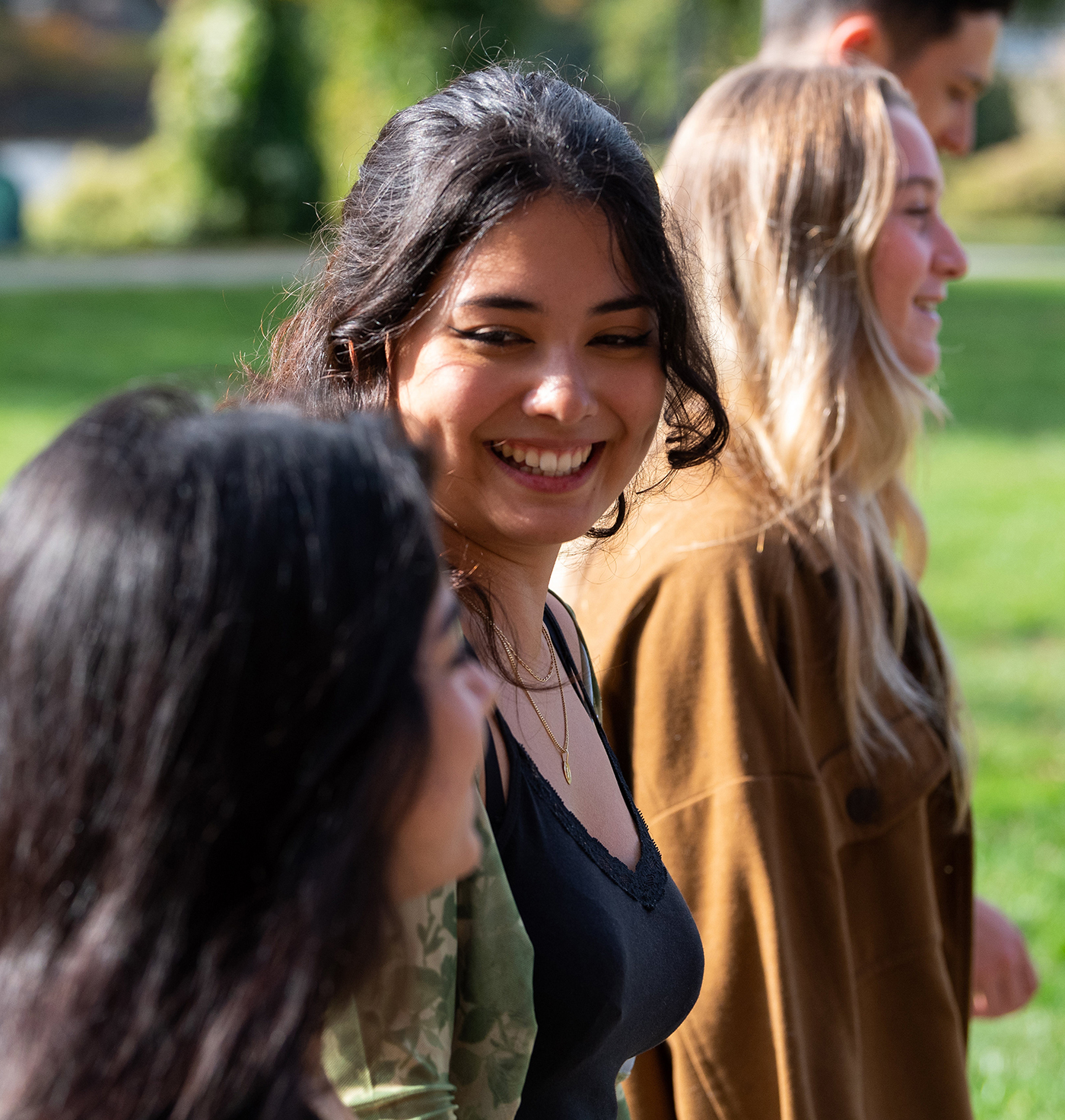 A group of students walk and talk in the sunshine on campus.