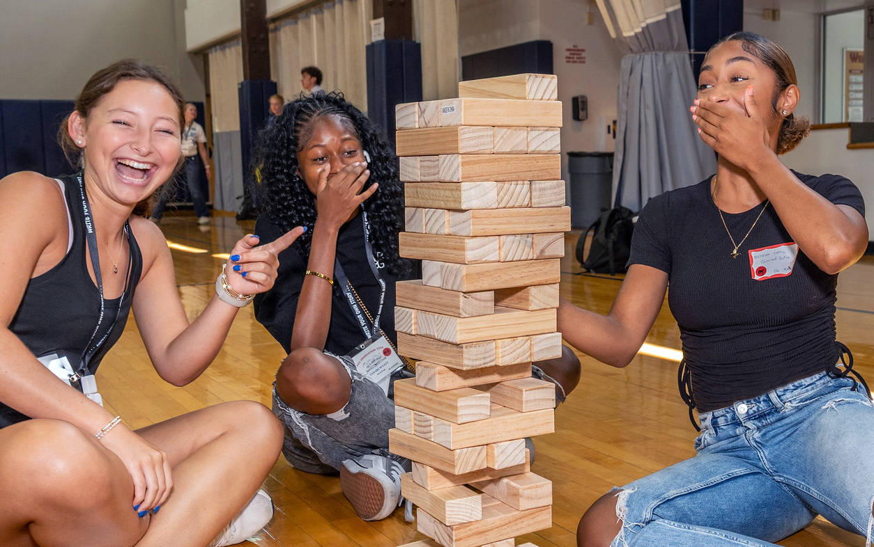 Three female students giggle as they play a giant game of Jenga.