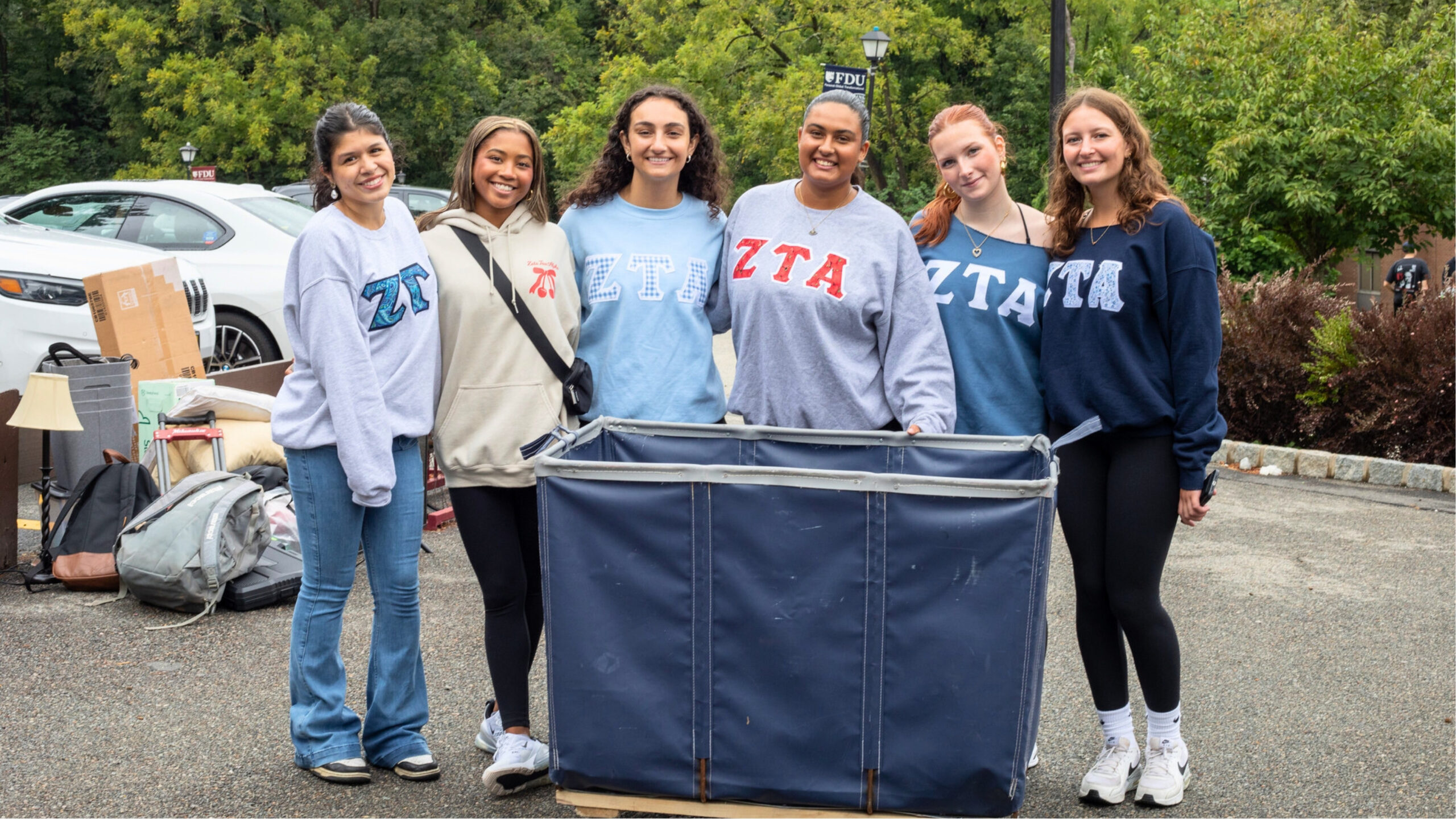 a group of college students smile for the camera. they all wear ZTA sweatshirts and stand behind a move-in wagon.