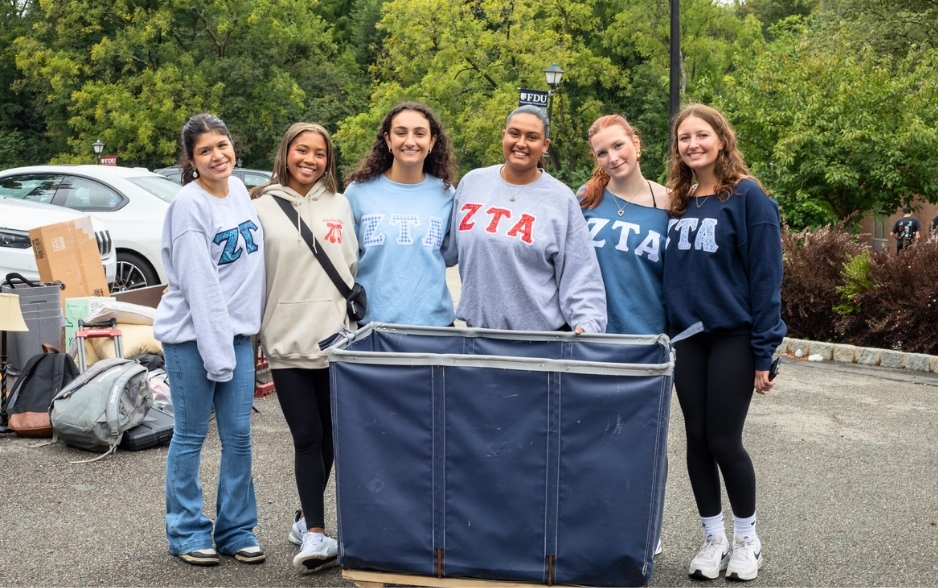 a group of college students smile for the camera. they all wear ZTA sweatshirts and stand behind a move-in wagon.