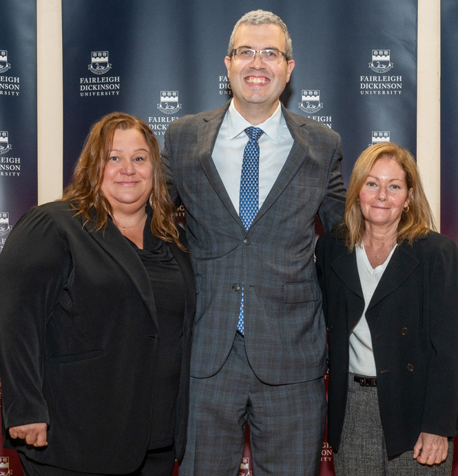 Three people pose for a photo together in front of a backdrop.