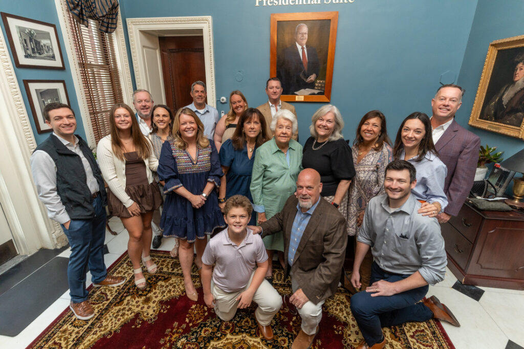 The Mertz Family gathered in front of a portrait of Frank Mertz.