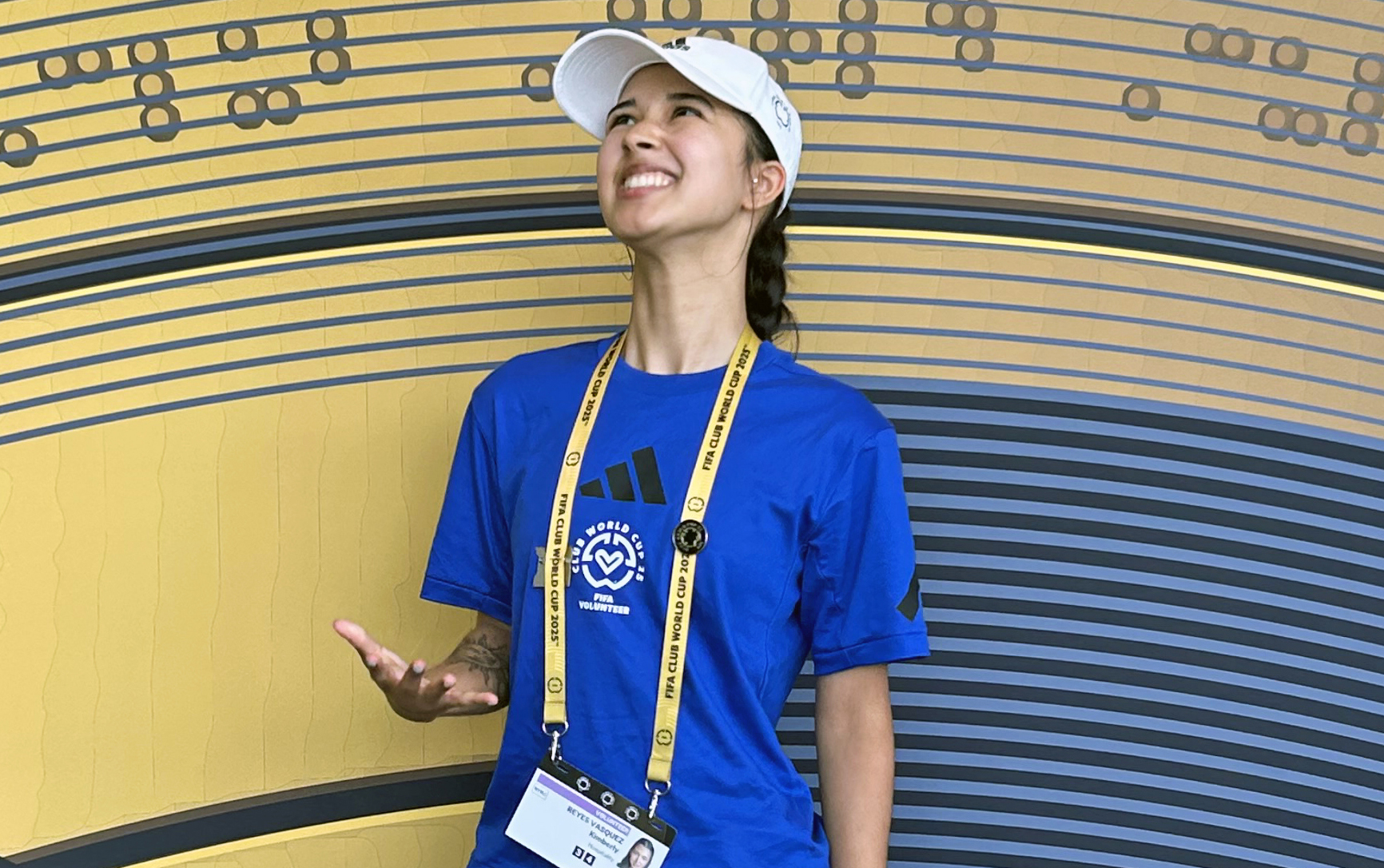 A young woman in a FIFA volunteer uniform throws a soccer ball in the air.