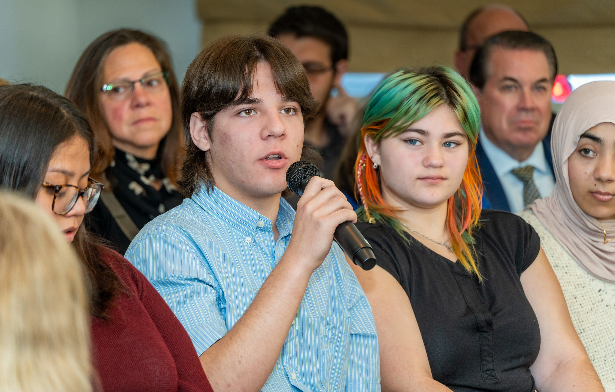 A student with a microphone asks a question at an event.