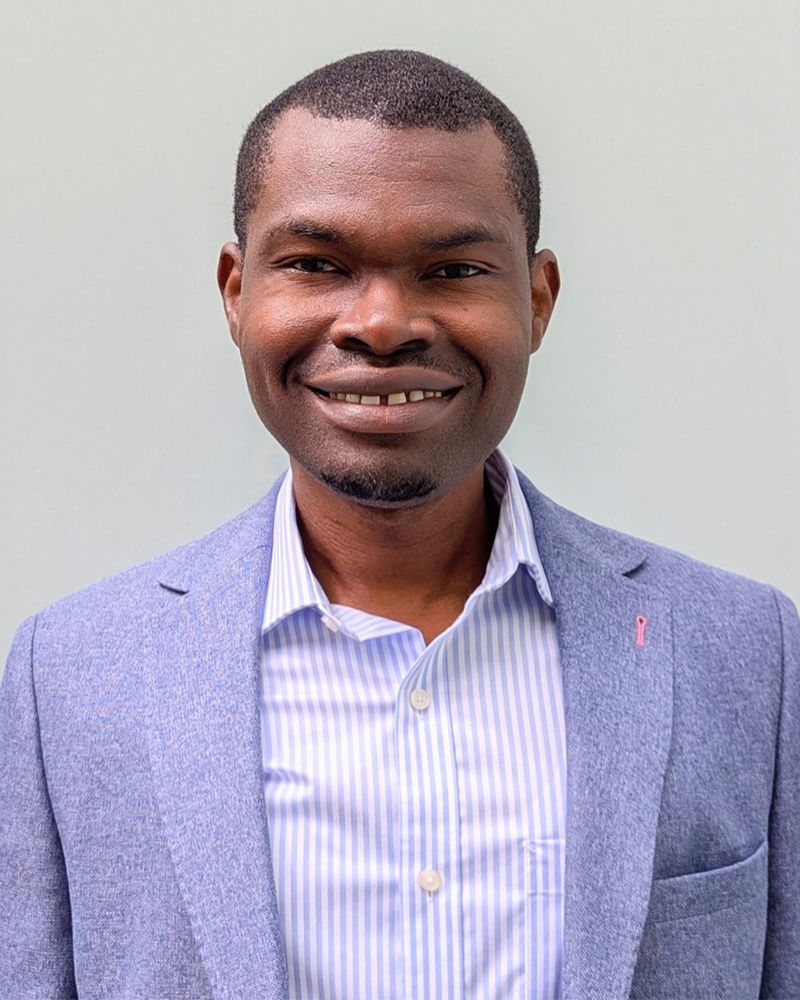 a portrait of a man. he wears a purple suit jacket.