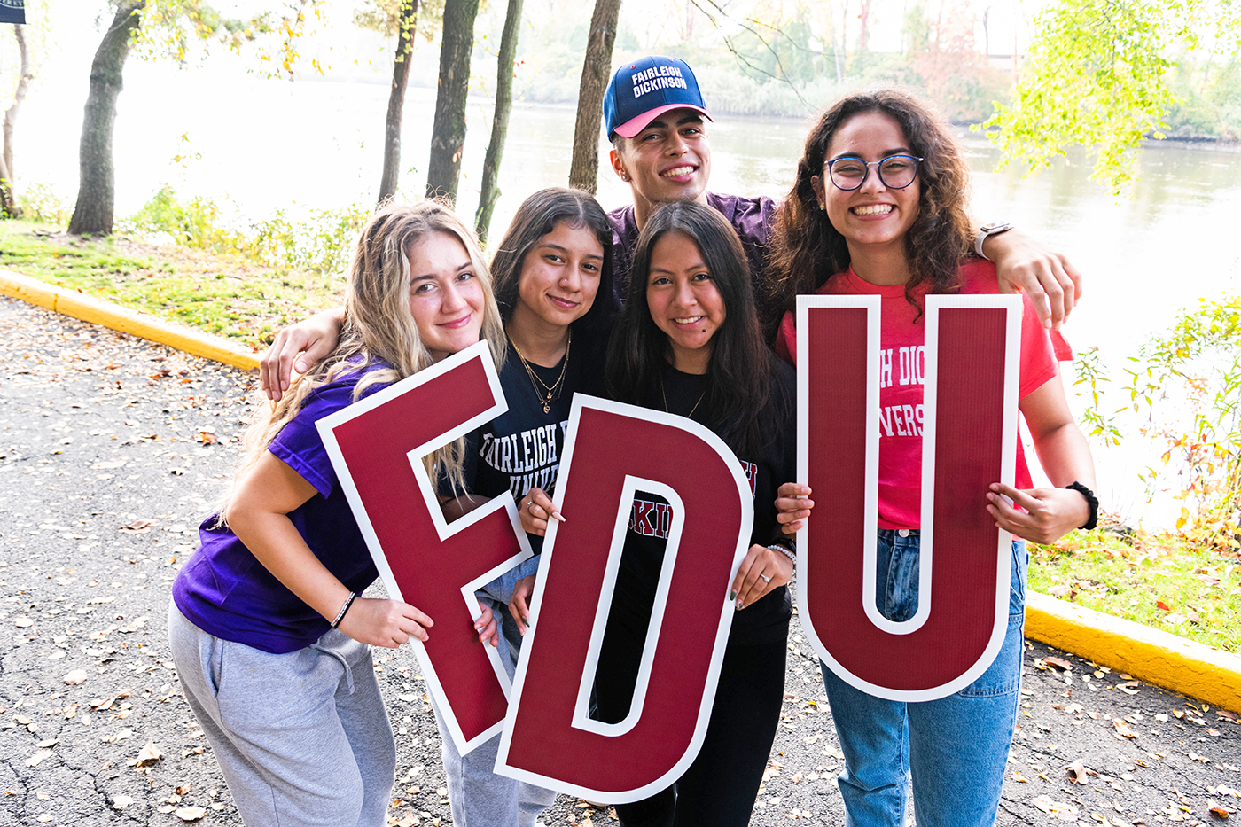 A group of students hold up FDU letters. They stand outside near the Hackensack River.