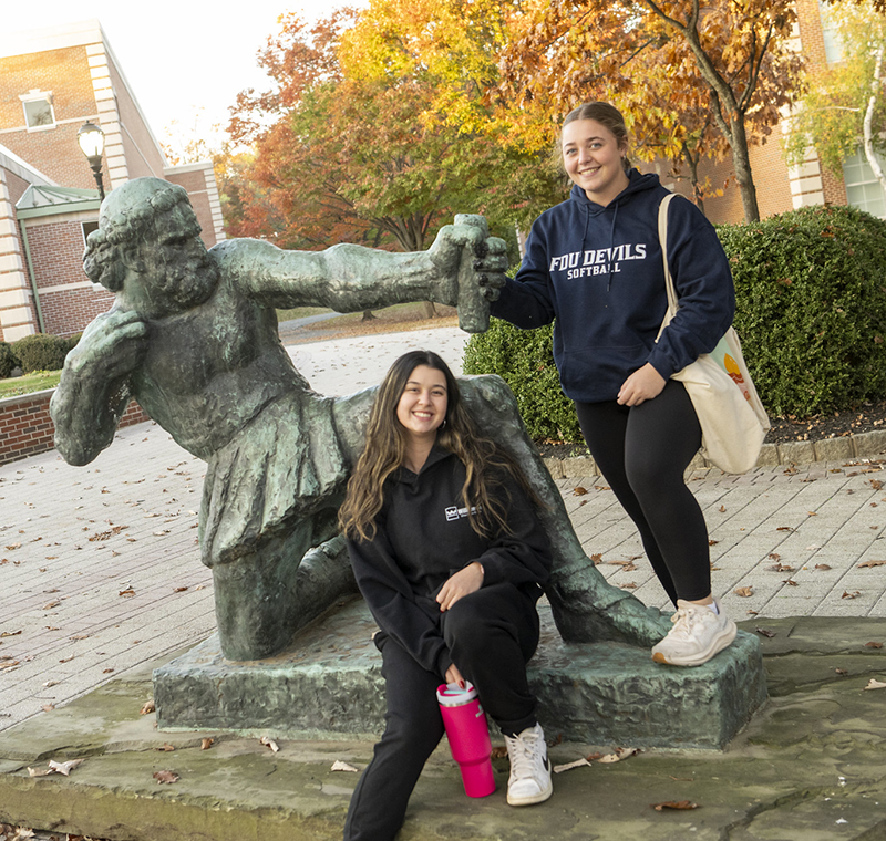 Two female students pose with a statue of Ulysses on the Florham Campus.