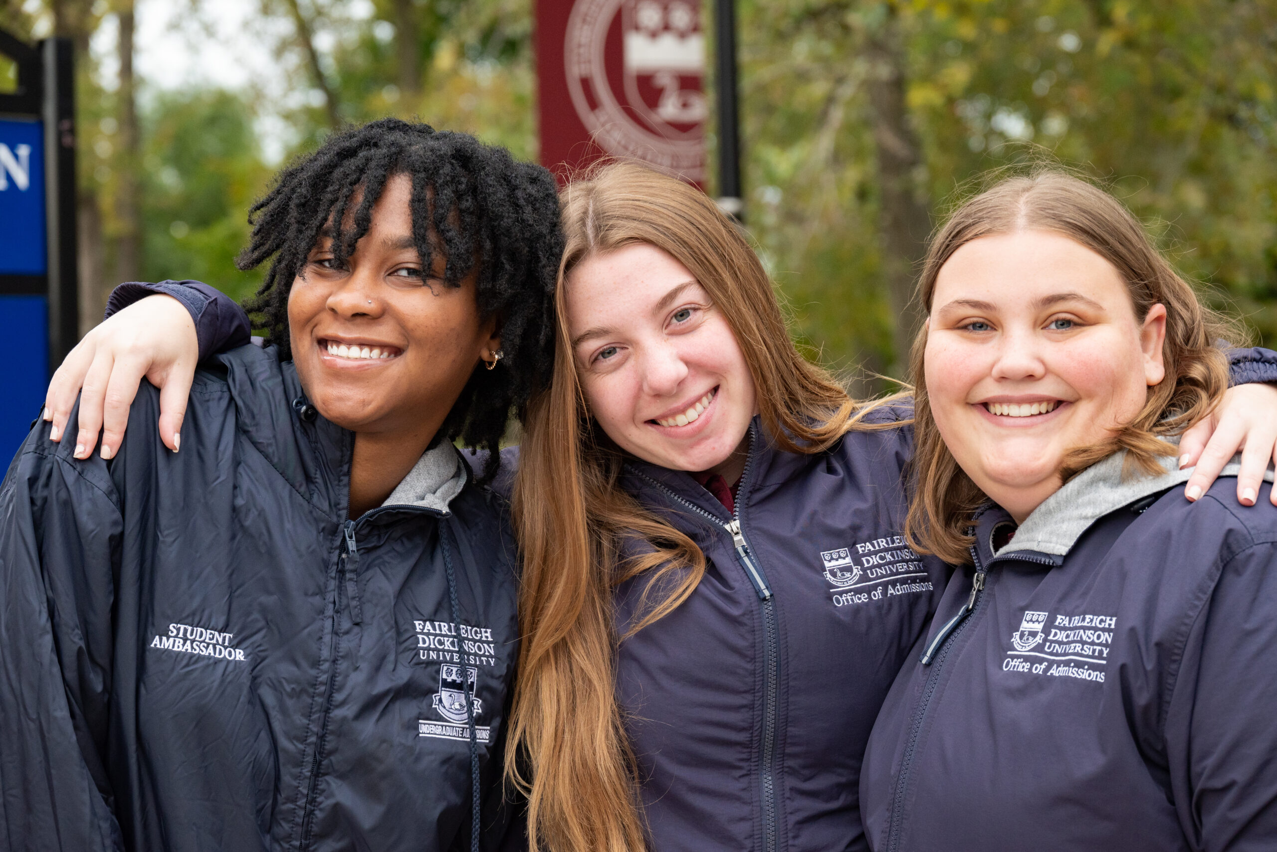 three student ambassadors side-hug each other and smile at the camera.