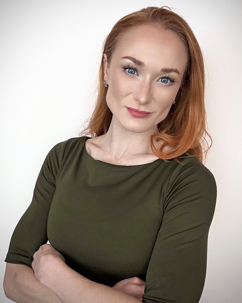 a portrait of a woman. she wears a green top and crosses her arms.