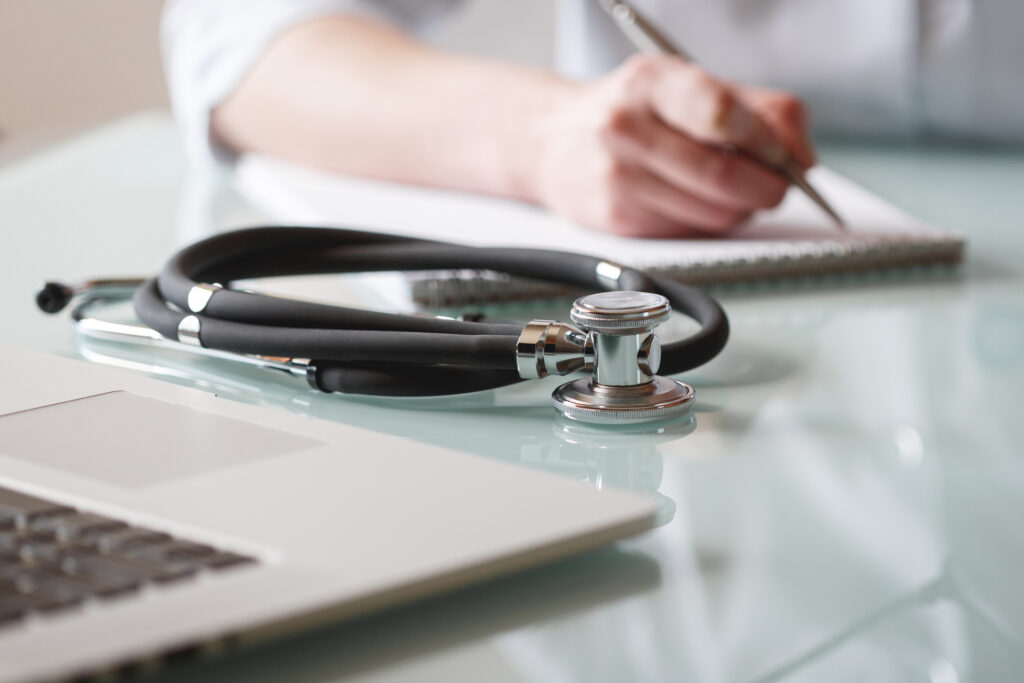 A stethoscope is lying on a table while doctor makes notes in a notebook. Medical care concept