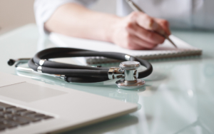 A stethoscope is lying on a table while doctor makes notes in a notebook. Medical care concept