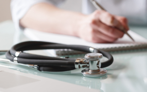 A stethoscope is lying on a table while doctor makes notes in a notebook. Medical care concept
