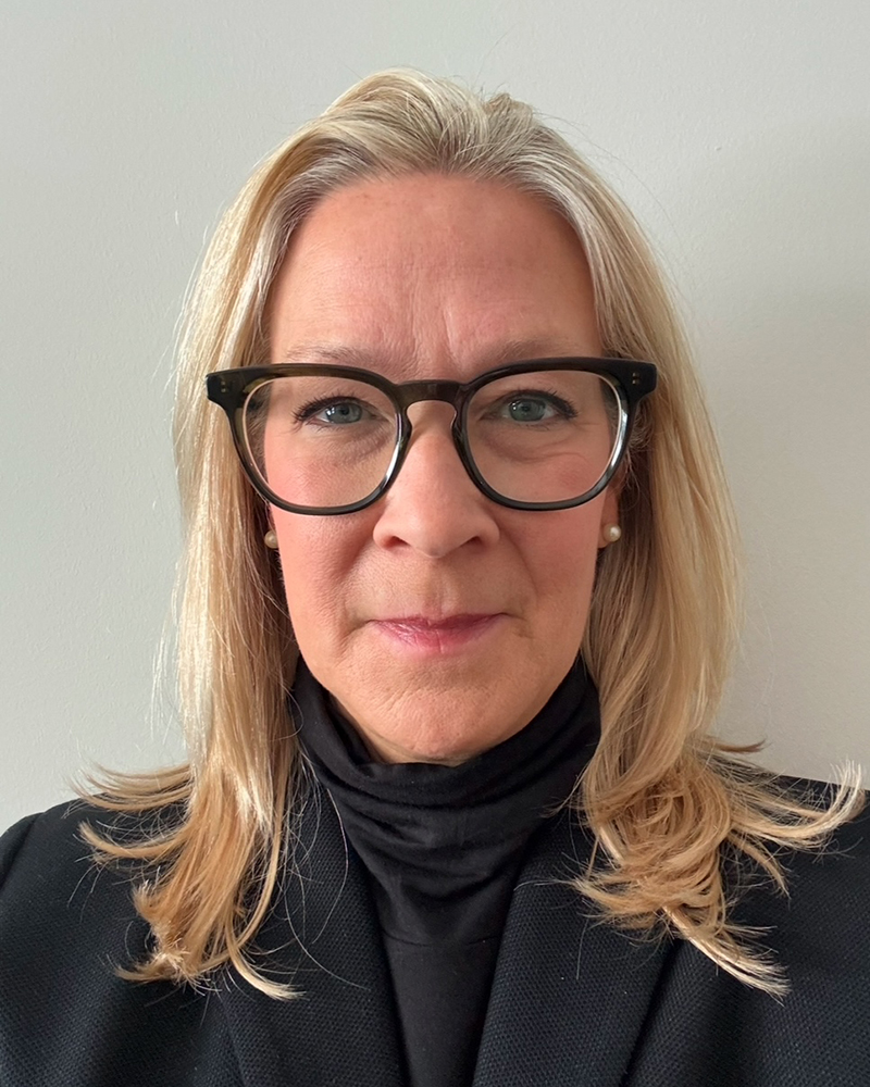 a portrait of a woman. she wears glasses, a black turtleneck and a black blazer.