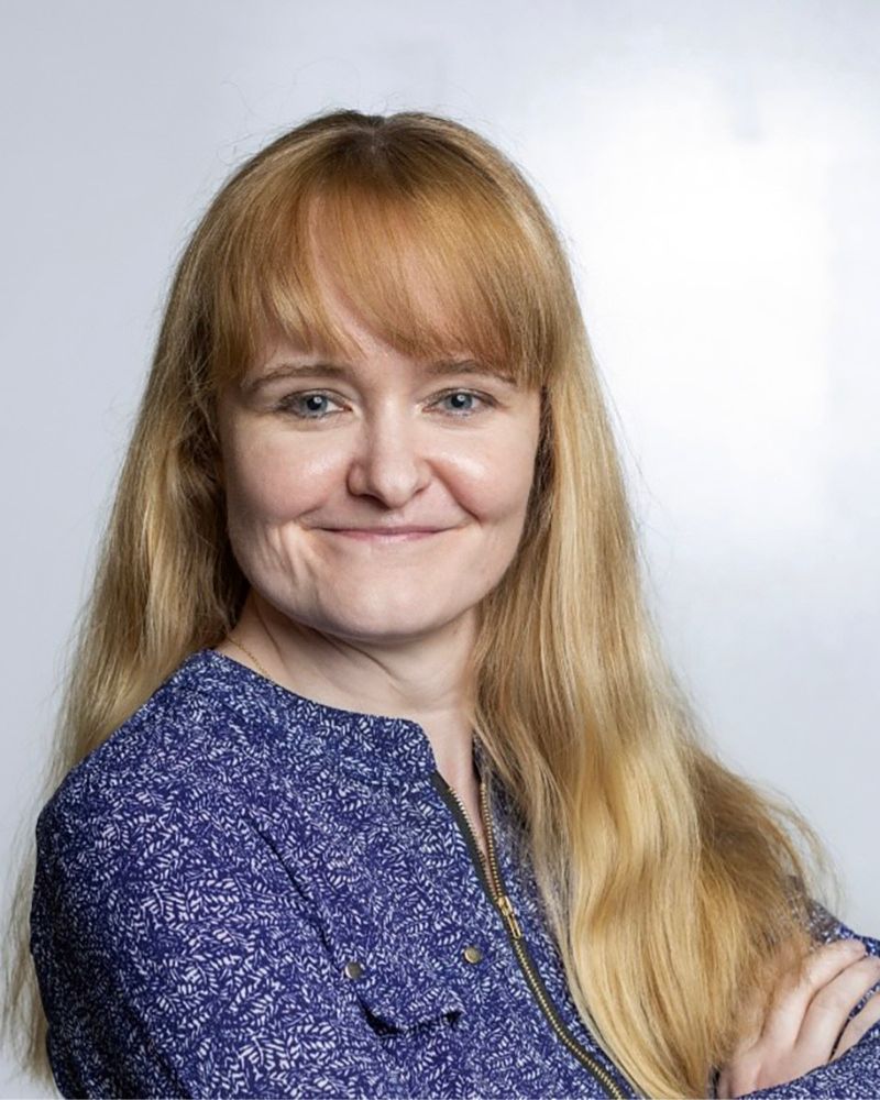 a portrait of a woman. she wears a blue blazer and crosses her arms.