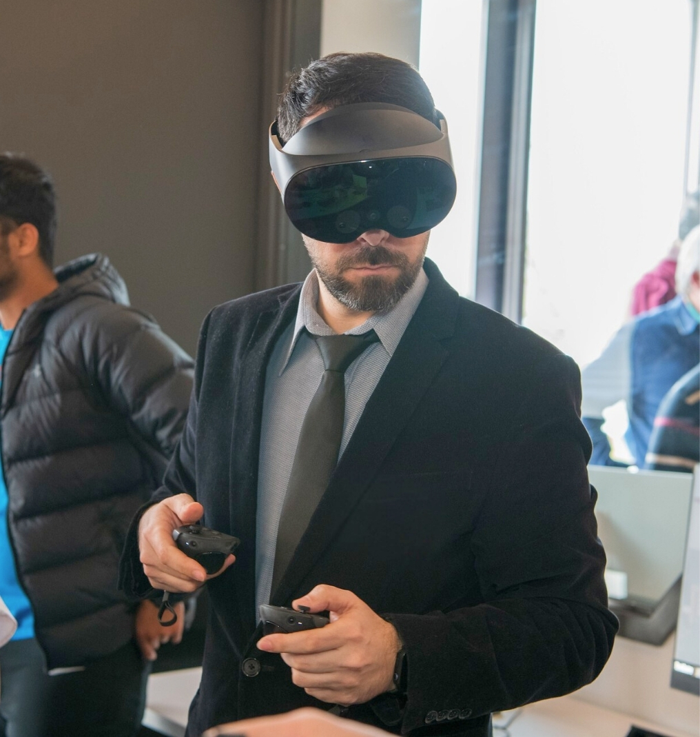 a man wears a suit and a VR headset. he holds two controllers.