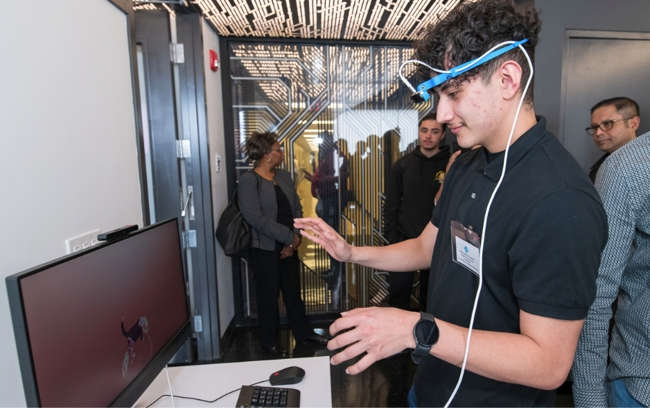 a college student wears a motion headset. he waves his hands at a computer screen.