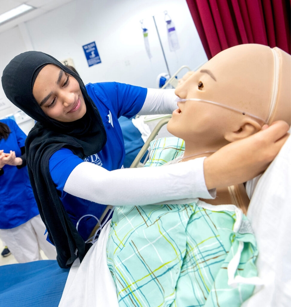 a nursing student puts a nasal cannula onto a patient mannequin.