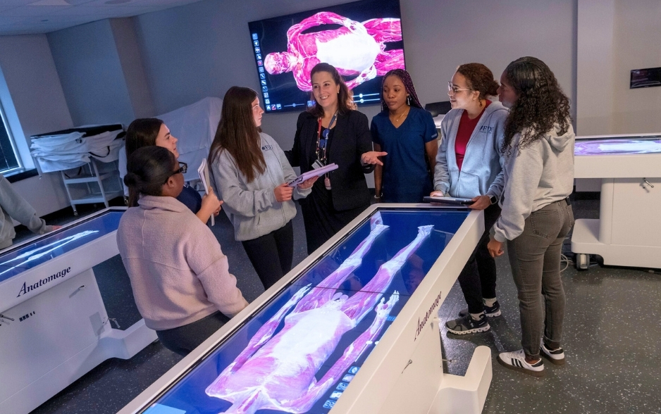 college students and a professor discuss a topic while standing around a digital model of a human muscle system.