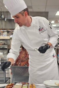 Man in chef's attire working on a dish