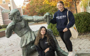 Two female students pose with a statue of Ulysses on the Florham Campus.