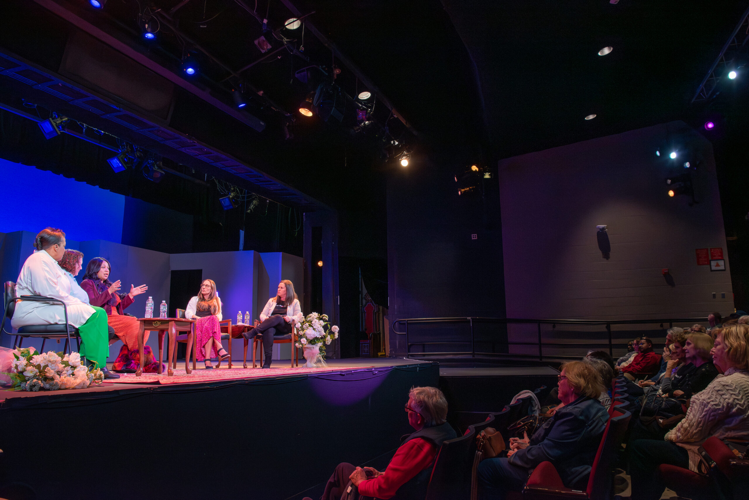 Five women on stage speak to an audience.