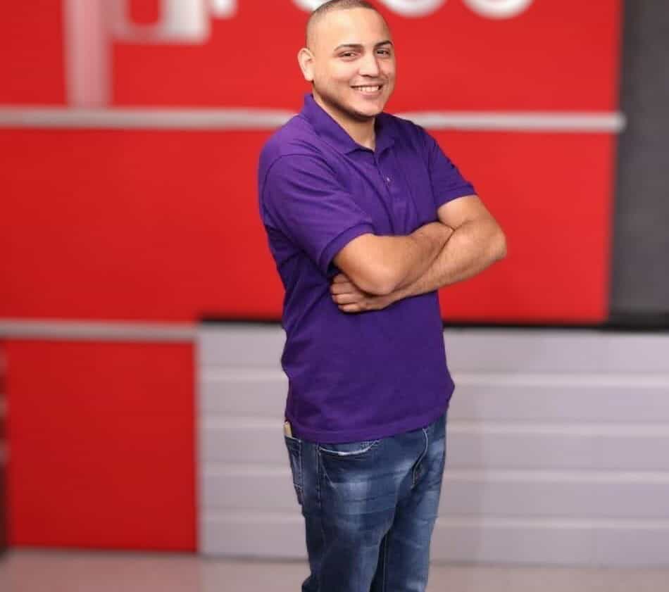 Picture of Angel Camacho, standing with arms folded in a purple polo and blue jeans.