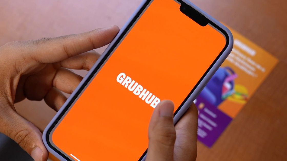 a phone with the Grubhub app open on it. there is a Grubhub discount flyer in the background.