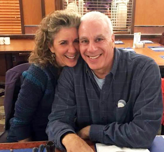A couple sits at a table at a restaurant and cuddles close.