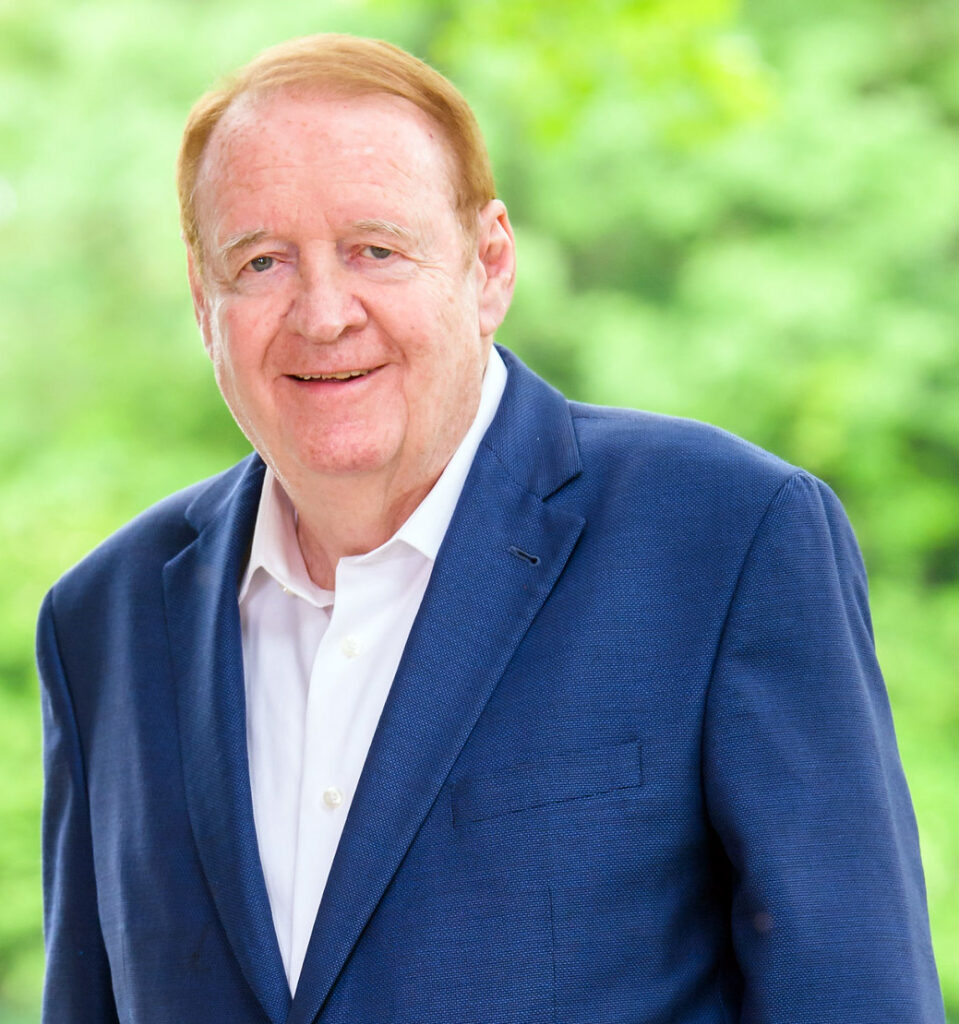 Portrait of a man in a suit standing outside in the trees.